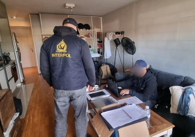 Agente de Interpol junto al hombre detenido en Argentina por un pedido de captura internacional vinculado con presunto fraude migratorio.